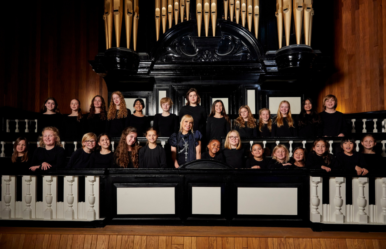 The Sky Kids choir and Paloma Faith are stood in front of an organ in a recording studio smiling